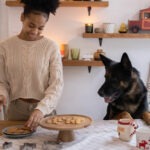 Frau legt die selbstgebackenen Hundekekse auf einen Teller und der Hund schaut zu