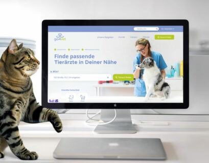 Katze sitzt vor einem PC Bildschirm auf dem eine Plattform für Tierarztsuche dargestellt ist