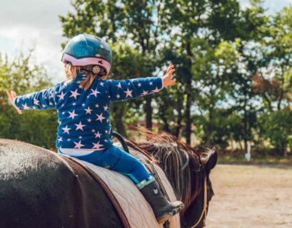 Kind sitzt auf einem Pferd und macht therapeutisches Reiten