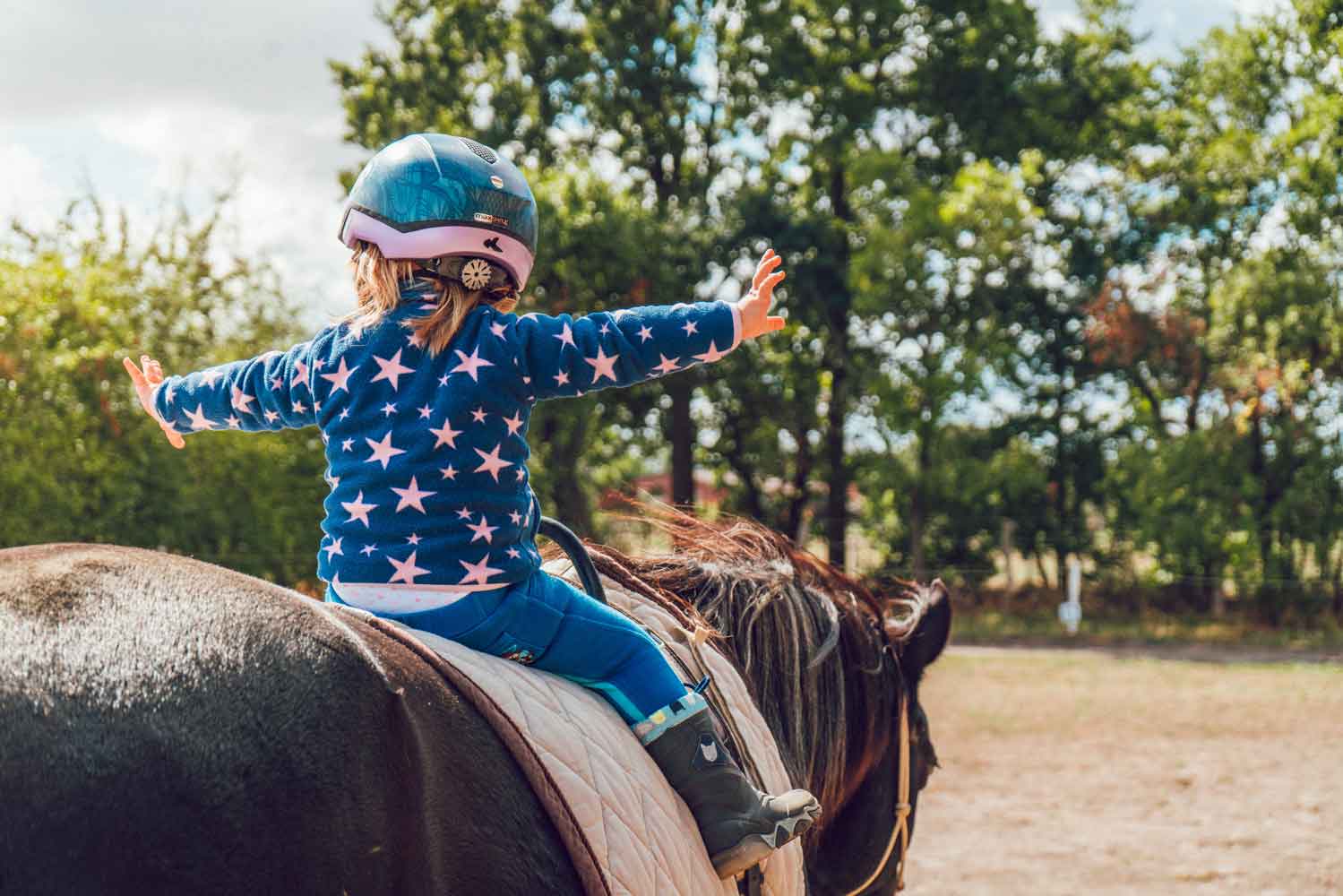 Kind sitzt auf einem Pferd und macht therapeutisches Reiten